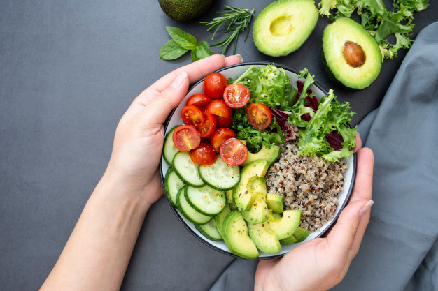 Healthy food. Womans hand holding budha bowl with quinoa, avocado, cucumber, salad, tomatoe, olive oil. Clean eating, diet food. Lose weight. Dark background.